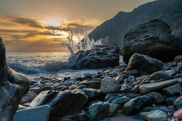 Wave hits the rocky shore by the mountain at sunset in Catalina Island