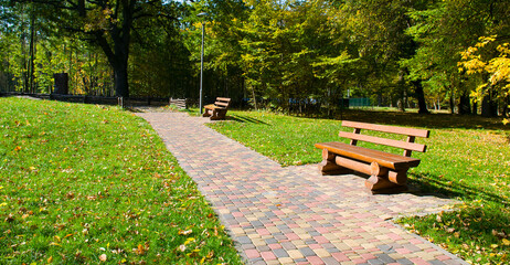 Beautiful garden with wooden benches and a green lawn. Wide photo.