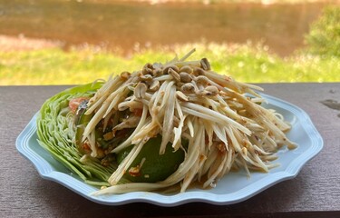 Papaya salad on a wooden table with blurred​ river, the popular dish in Thailand.