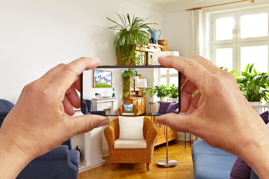 Augmented reality concept: hands holding smart phone with AR interior decoration app, visualising the living room with added poster and pillow print.