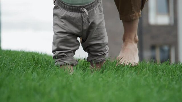 Medium close-up low section shot of unrecognizable mother and baby walking barefoot on lawn grass
