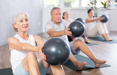 Fototapeta na wymiar Portrait of mature people doing exercises for press with pilates ball during group class in fitness studio