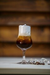 Glass of iced coffee with cream against a wooden wall