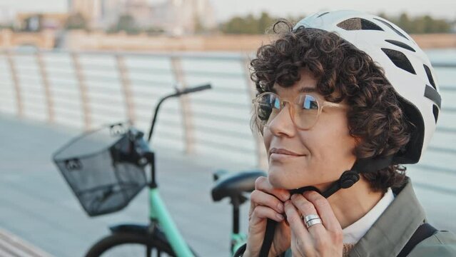 Close-up portrait Caucasian female office worker sitting outdoors in morning putting on bicycle helmet