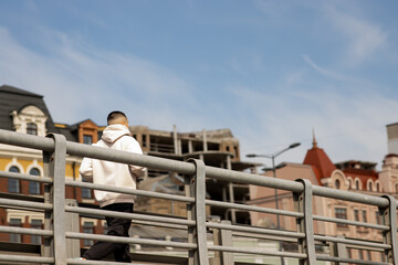 A young man runs across the bridge against the backdrop of the city. A guy in a white hoodie is going for a morning jog around the city.