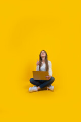 Pointing up copy space, full body young caucasian girl sitting ground pointing up copy space. Young brunette office worker IT woman holding modern laptop. Isolated yellow background. Working on pc.