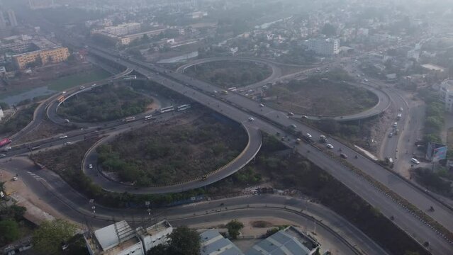 Aerial view of the cloverleaf interchange of Maduravoyal flyover Bridge with smooth-flowing traffic under the smoggy and hazy morning light, Chennai, India