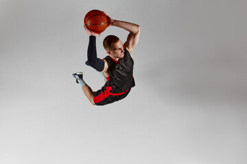 Dynamic image of concentrated young man, basketball player throwing all in a jump against grey studio background. Aerial view. Slam dunk. Concept of professional sport, competition, action and motion © master1305