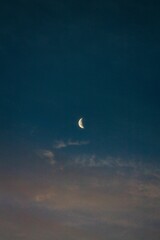 Vertical shot of the crescent moon on the blue sky background in the evening