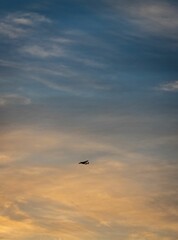Vertical shot of a plane flying in the sky with clouds at sunset.
