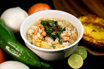 Closeup of a Mexican soup on a white bowl with vegetables near it