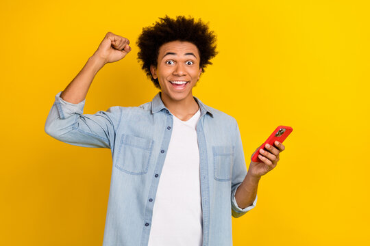 Photo of funky lucky guy dressed denim shirt rising fist texting apple iphone isolated yellow color background