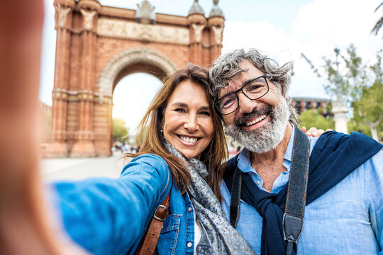 Married couple taking selfie in front of Triumphal Arch in Barcelona, Catalonia, Spain - Husband and wife enjoying romantic moment together at summer holiday in Europe