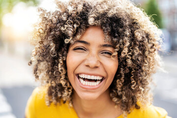 Happy afro american young woman smiling at camera outside - Close up portrait of brazilian female laughing on city street - Life style and positive vibes people concept - obrazy, fototapety, plakaty
