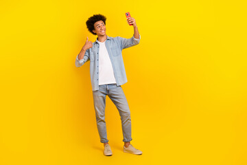 Fototapeta premium Full length portrait of handsome guy hold smart phone take selfie demonstrate thumb up isolated on yellow color background