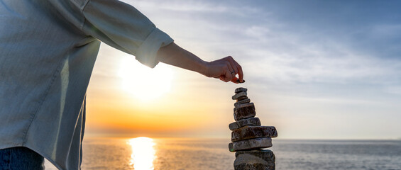 Woman building a cairn pyramide on the seashore at sunset. Zen relaxation and meditation concept