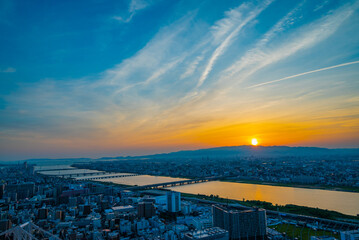 夕焼け空、綺麗な夕陽が沈もうとする都会、そして川の水面に映る陽の光が美しい写真。ビルの屋上から見下ろした風景