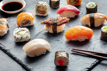 Sushi with chopsticks and soy sauce. Rolls, maki, nigiri on a black background, Japanese food. Salmon, tuna, eel, shrimp and other seafood with rice on a plate at an Asian restaurant