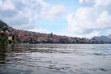 Obraz premium Picturesque town at lake Como. Colourful motley Mediterranean houses at the beach coastline among green trees. Popular health resort and touristic location. Summer day landscape.