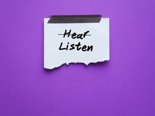 Stick note on purple background with handwritten text HEAR crossed off to LISTEN, means to be better listener with empathy not just hearing, see the world in speaker eyes and understand their emotions