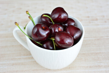 heap of ripe dark cherries in the white cup isolated, copy space 