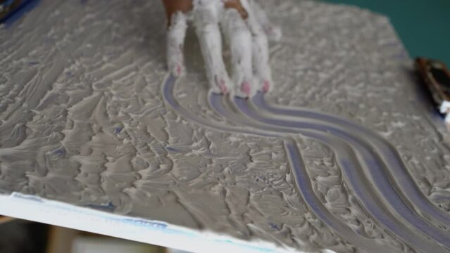 Female artist draws with her hands on the canvas, she creates emotional textured oil painting with fingers. Painter creating abstract modern art
