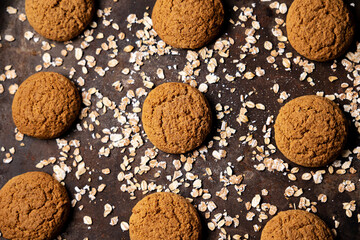 Craft and rustic four oatmeal cookies. Dark food aesthetics, black background with several oat flakes.