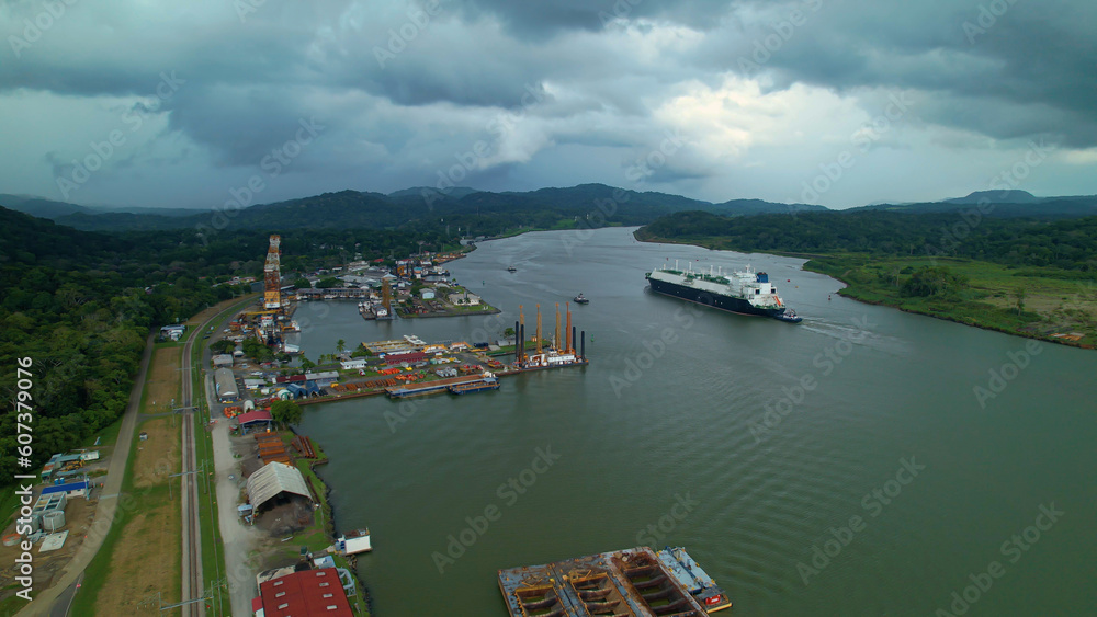 Wall mural dark rain clouds rolling over port and cargo ship passing through panama canal