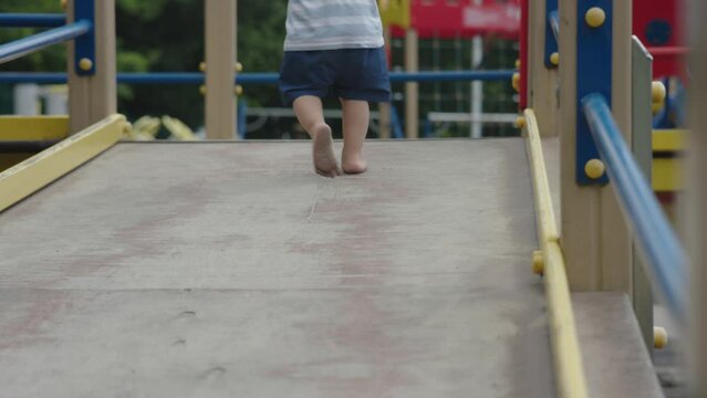 small child bare feet walking on playground summer day outdoors. bare legs baby kid blue shorts on dirty coating. Concept of hardening children, health, development of feeling, nature, orthopedic