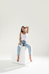 Obraz premium Full length photo of confident young woman in casual outfit, in white tank top and jeans, posing in studio, looking at the camera
