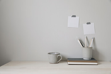 Office table. Empty desk with office supplies and beige wall copy space. Pencils holder, notebooks and cup of coffee. Blank note pad mockups, striped washi tape. Elegant interior, work break concept.