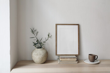 Cup of coffee, books. Empty vertical picture frame mockup on old books. Wooden desk, table. Vase...