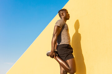Young man doing stretching exercise outside. African man training outside.