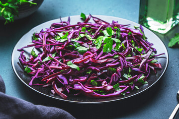 Healthy vegan vegetable salad with red cabbage, parsley and olive oil on blue kitchen table...