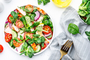 Healthy fresh salad with grilled chicken slice with cherry tomatoes, cucumber, red onion, lamb lettuce and sesame seeds on white table background, top view