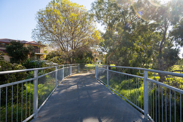 A pedestrian boardwalk with a metal handrail near some Australian residential houses. Concept of a nature trail in the neighborhood, footpath in the suburb. A quiet walkway in Point Cook Melbourne.