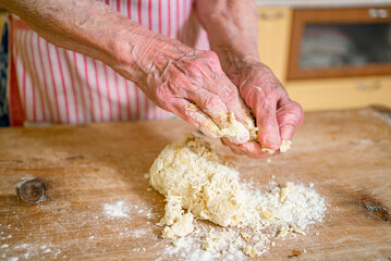 grandmother kneads dough, prepares noodles in the kitchen at home. Senior woman hands are rolling out dough in flour with a rolling pin in her home kitchen. 