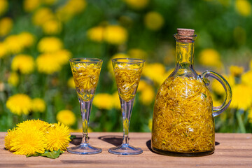 Homemade dandelion flowers tincture in two glasses and in a glass bottle on a wooden table in a...