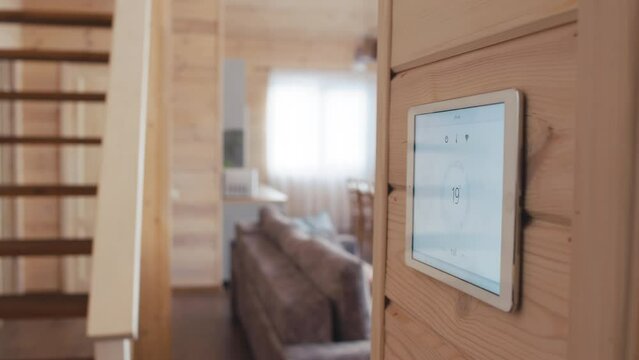 Selective focus shot of Caucasian woman living in modern wooden house equipped with home automation system changing indoor temperature using tablet on wall