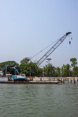Fototapeta premium Large water crane on a river. Industrial riverbank with a water crane and beautiful nature. Riverbank full of concrete pillars. Beautiful southeast Asian river and blue sky shot. Coast of a river.