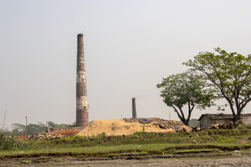 Fototapeta na wymiar Scenic scenery of a brick kiln and sky. Brick kiln and village area scenery with blue sky. A beautiful rural area on the bank of a river. Huge sand and brick stack and green trees.