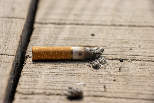 Burning cigarette close up on a broken wooden surface. Cigarette on a wooden surface close up. Unhealthy smoking habit and cigar addiction. Nicotine addiction concept with a burnt cigarette and ashes.