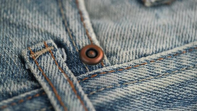 rivet on the front pocket of denim trousers and orange stitching on the edges of the fabric. rotation of the fabric of blue jeans in close up details. denim texture, abstract background.