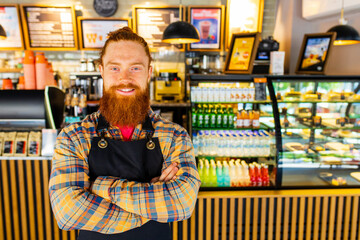 Professional barista young redhaired ginger bearded man in black apron working in coffee shop