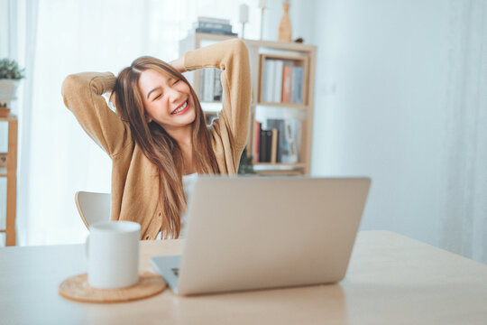 Happy positive young asian woman enjoying online communication at home, Female using wifi while video conferencing with friend and sitting in front of open laptop with a coffee mug.