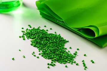 Green plastic granules near the polymer film. Raw material for the production of plastic products.