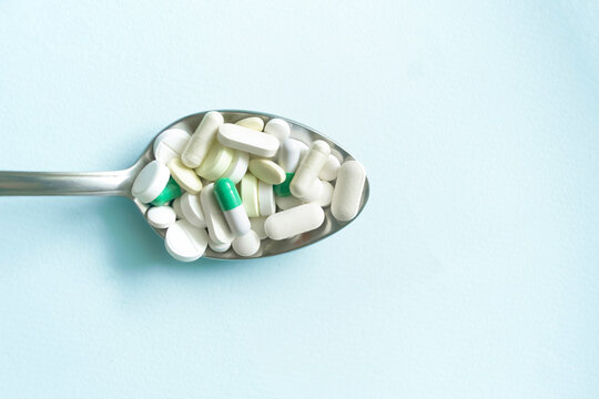 On a blue background lies a spoon filled with tablets and capsules. The benefits and harms of tablets. Traditional medicine - a lot of medicinal capsules and tablets in a metal spoon.