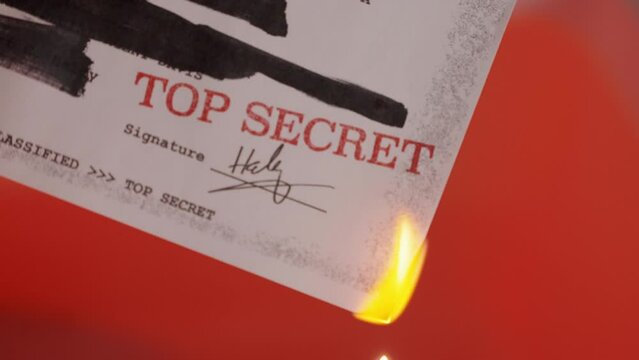 Top secret document with red official stamp and blacked out lines in set on fire. Classified and sensitive information with redacted text is burned with match. With red background. Eliminating paper