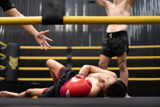Unconscious Asian boxer lay on floor referee counting down knockout in the ring at fitness gym. Boxing is fighter sport training need body muscular strength, power fist and sweating to become champion
