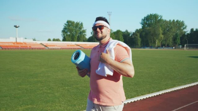 Expressive overweight cheerful motivated funny man in a great mood goes to train at the stadium.